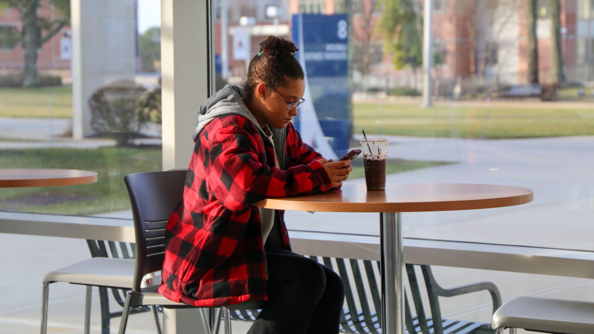 Student sitting alone at table on phone